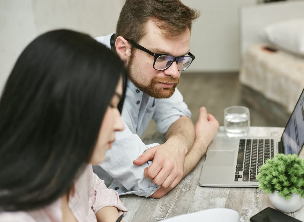 A man and woman sitting at a table reviewing documents on a laptop indoors.